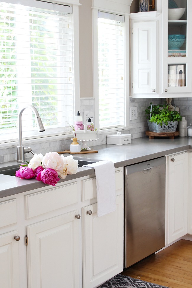 White farmhouse style kitchen with beautiful pink peonies in the sink. 